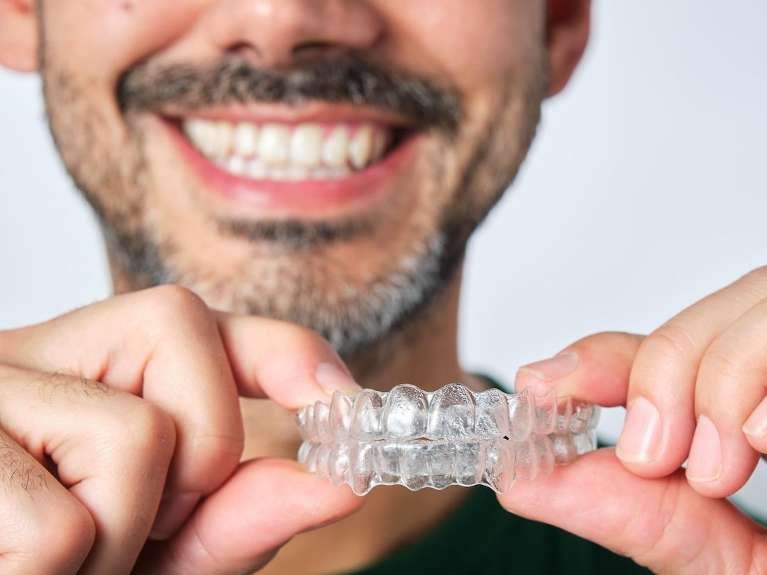 smiling man holding invisalign clear plastic aligners | invisalign dedham ma