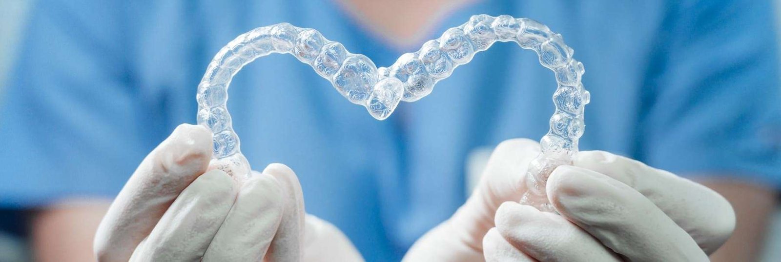 dentist holding two aligners shaped in a heart | dentist in dedham